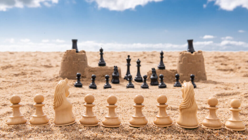 Chess pieces set up on sand.